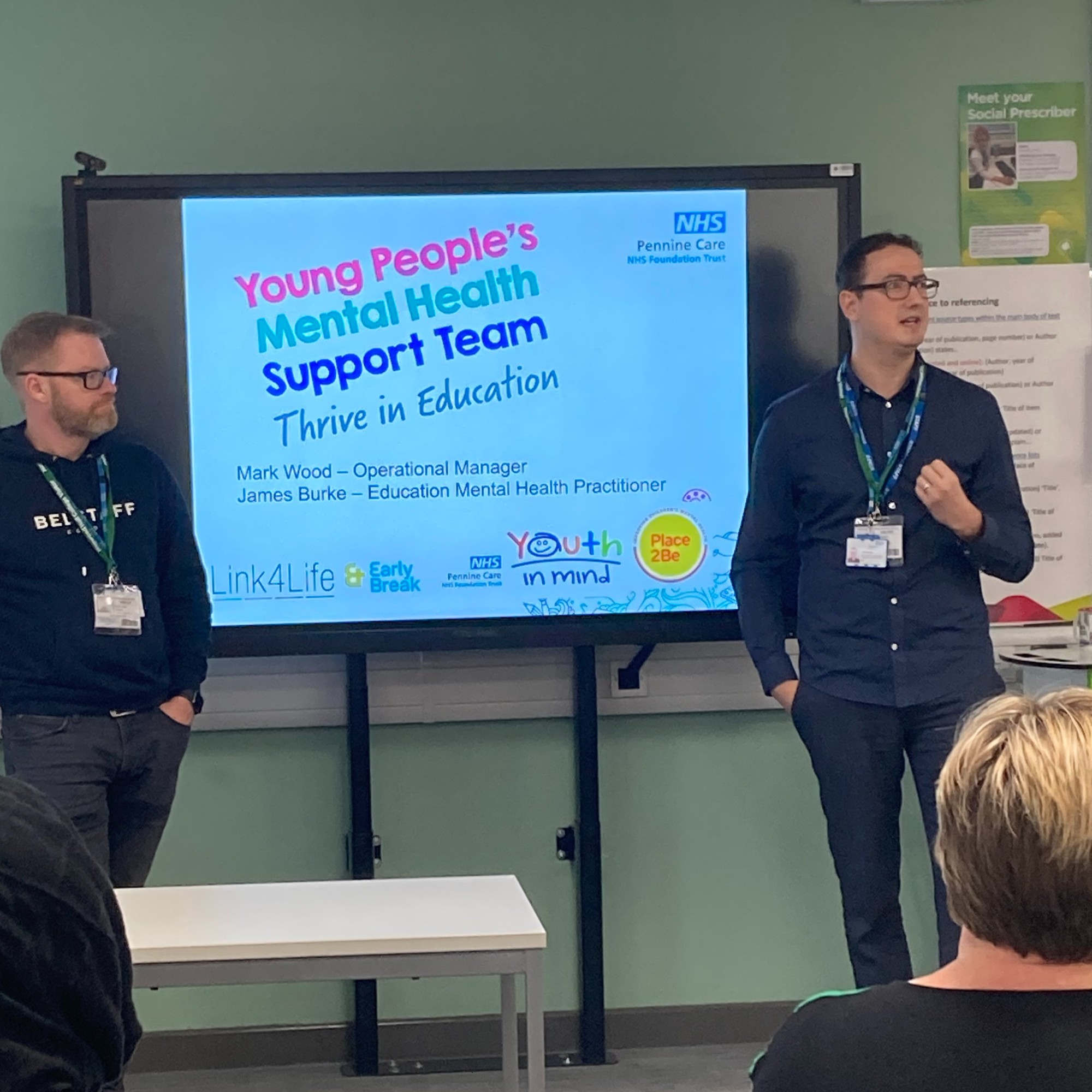Young people's mental health support team talking in front of a classroom.jpg
