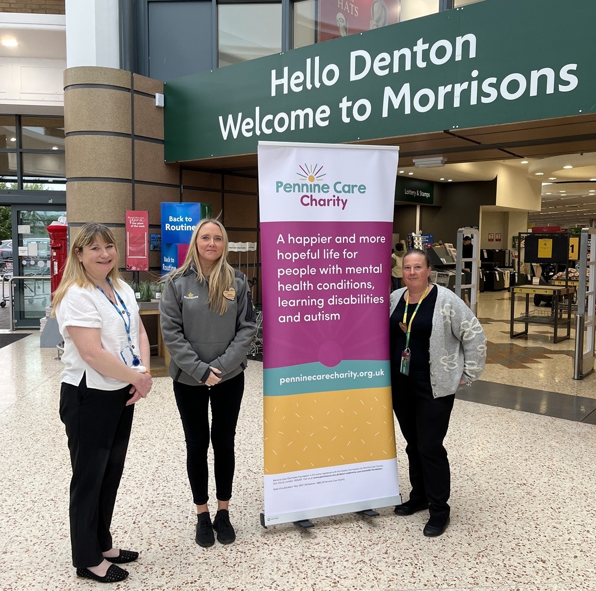 Three people standing next to a Pennine Care Charity banner in the entrance to Morrisons in Denton